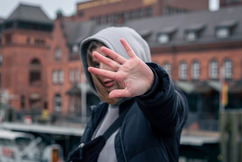 A woman's hand with rings covers her face on a blurred background, an urban portrait.