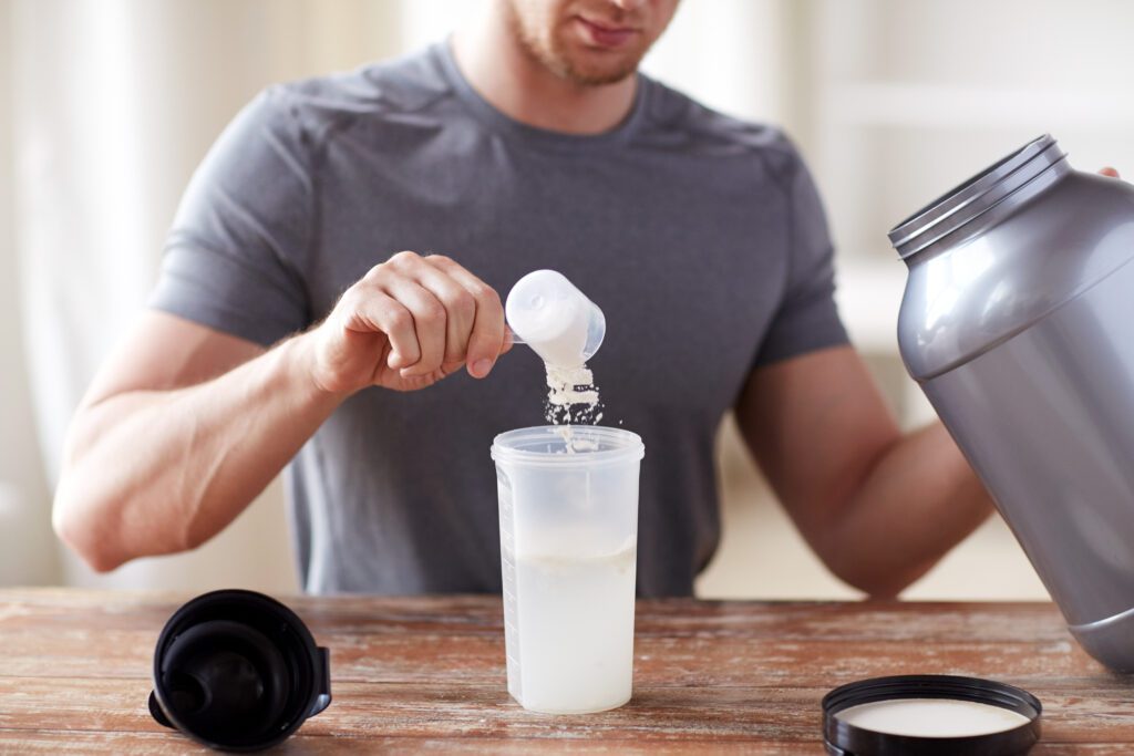 sport, fitness, healthy lifestyle and people concept - close up of man with jar and bottle preparing protein shake creatine
