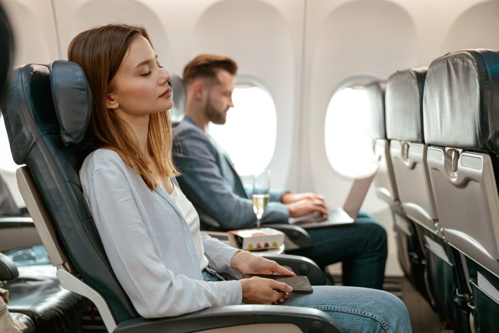 Female traveller sitting in passenger chair and holding mobile phone while sleeping during flight